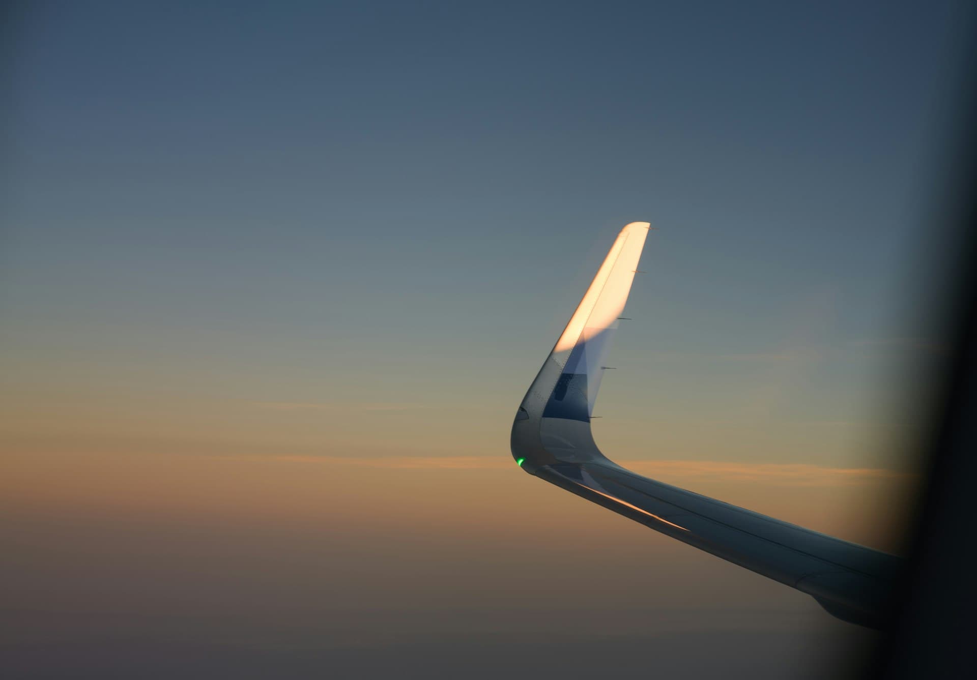 Airplane wing over a navy-and-gold gradient sky at dusk, seen from a window seat