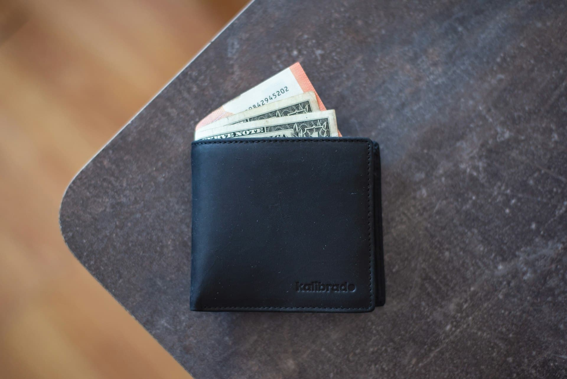 Black leather bifold wallet on a table with banknotes tucked inside