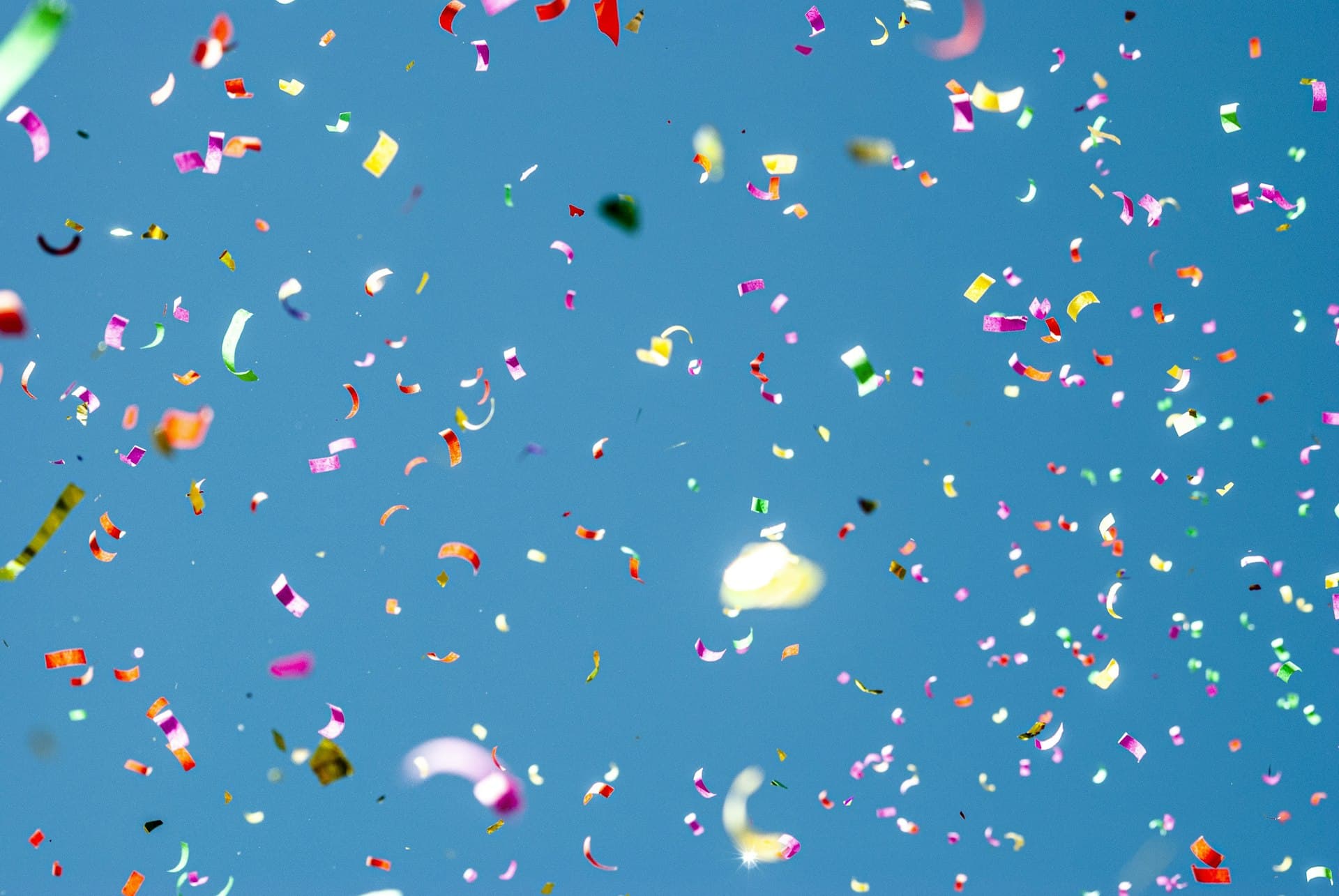 Colourful confetti falling against a clear blue sky
